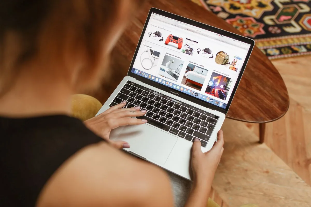 Pessoa fazendo compras online no notebook, sentada em uma mesa de madeira