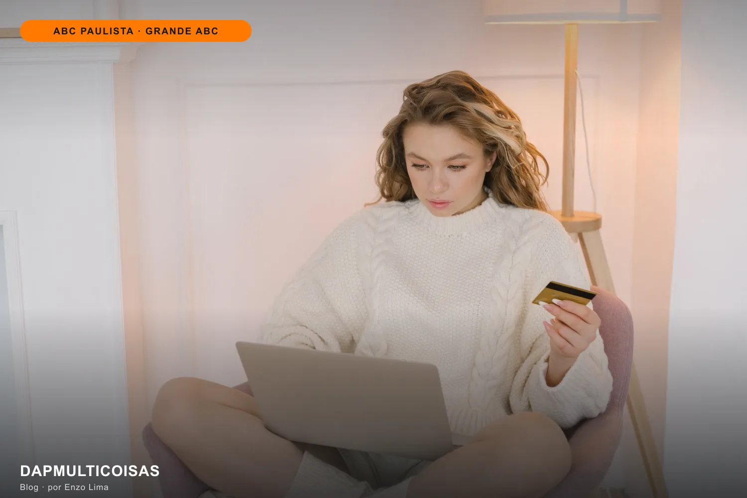 Mulher de suéter branco segurando o cartão e usando o notebook para comprar online